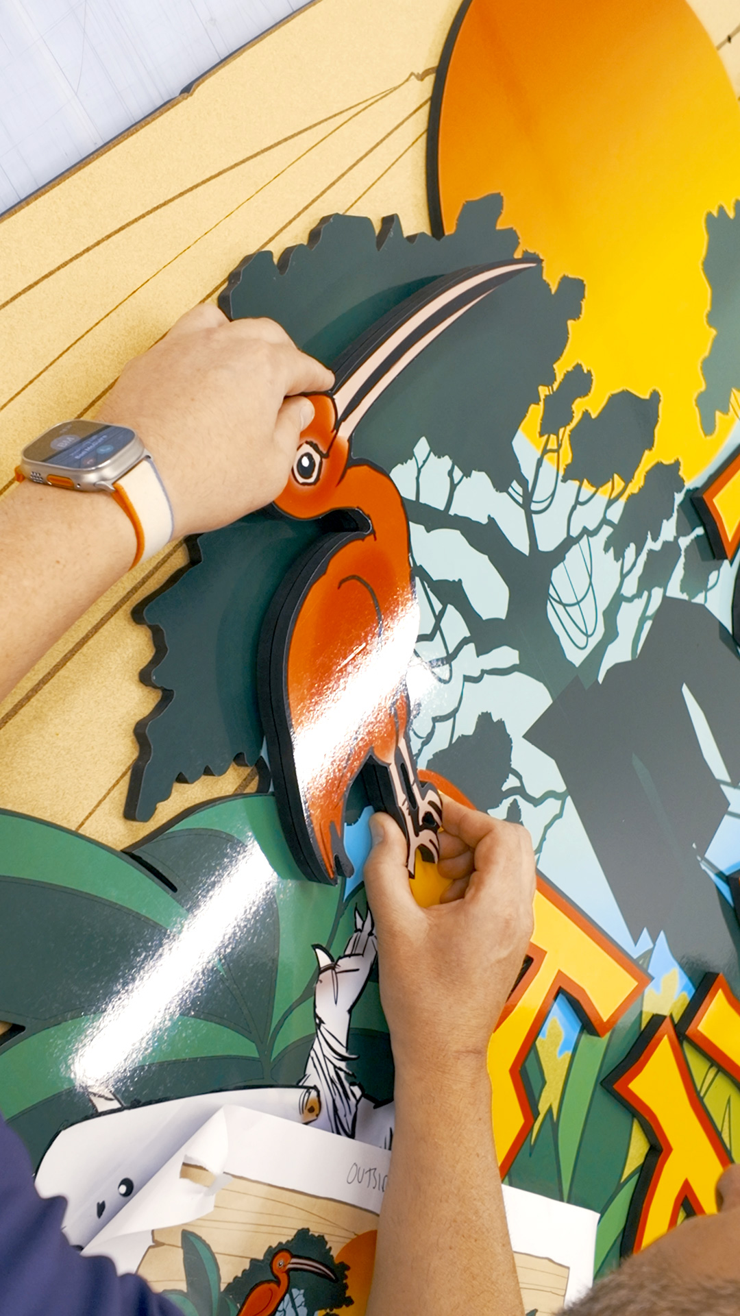 Technician attaching a raised bird graphic detail to the “Amazon Adventure” sign for Drusillas Park.