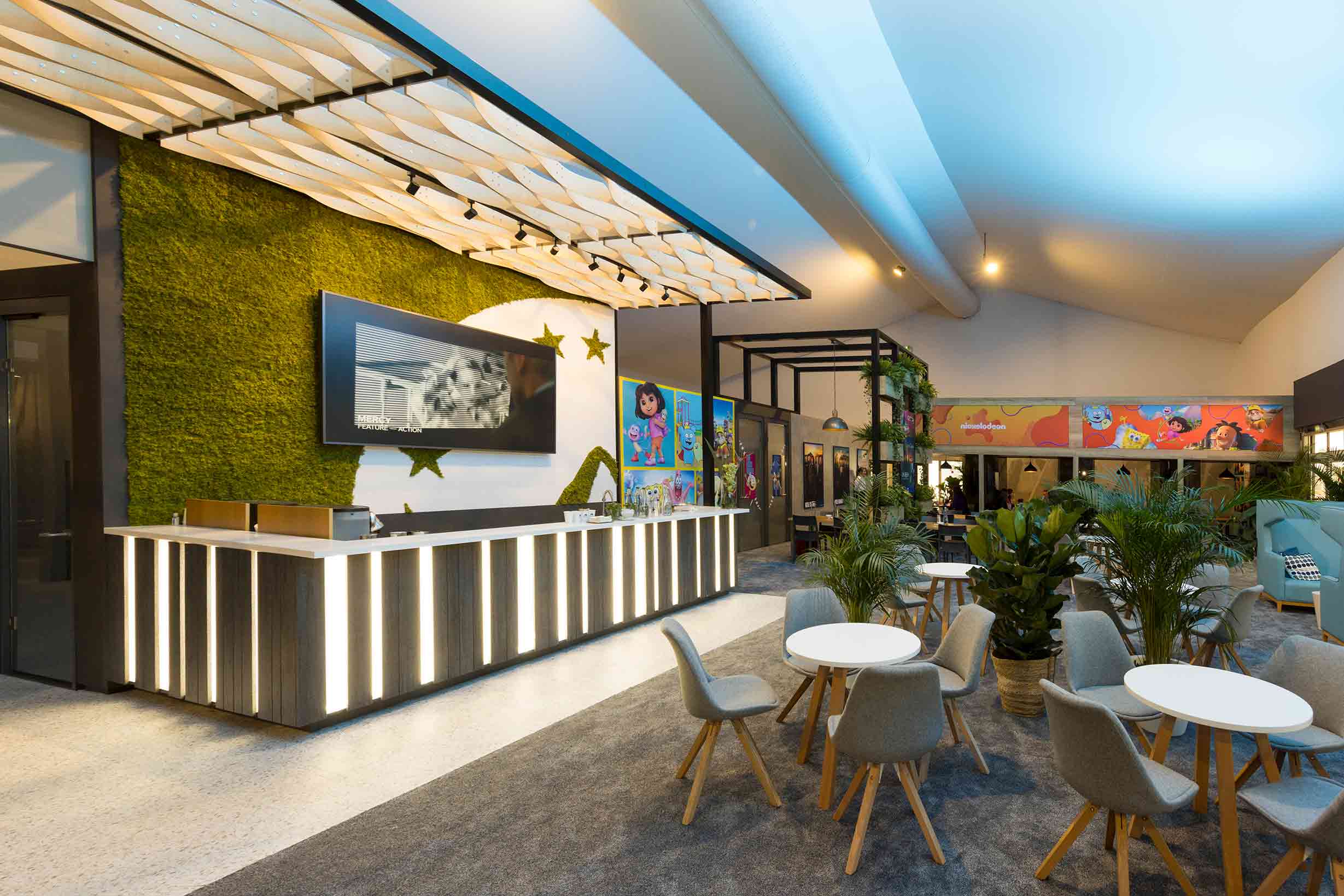 Paramount exhibition stand lunch hall with greenery, illuminated bar counter, and large-format character wall graphics by Beautiful LFP.